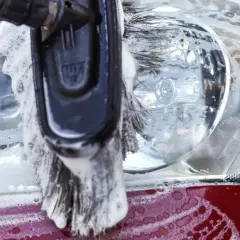 Cepillo con espuma limpiando el faro de una moto roja. Proceso de lavar moto en gasolinera.