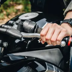 Mano sujetando el manillar de una moto, lista para accionar el freno motor.