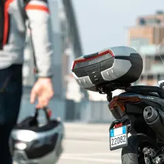 Hombre con casco en mano, listo para llevar su maleta en moto. La moto tiene un top case Givi Maxia.