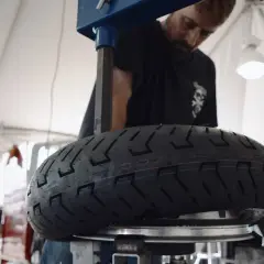 Mecánico revisa un neumático de moto con inscripción 100/90 r18 equivalencia.