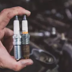 Mano sostiene dos bujías, una nueva y otra vieja. ¿Qué bujía lleva mi moto?