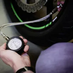Mano revisando la presión neumaticos moto con un manómetro. El neumático tiene detalles verdes.
