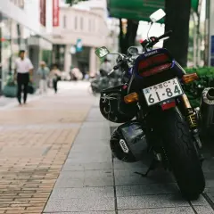 Una moto Yamaha aparcada en la acera, con dos cascos colgados. Al fondo, gente pasea por la calle.