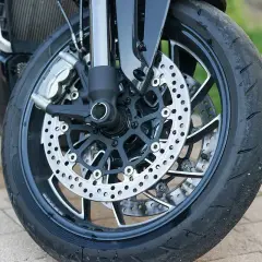 Primer plano de la rueda delantera de una motocicleta, con discos de freno perforados y pinzas. Se ve el neumático desgastado, listo para reparar rueda.