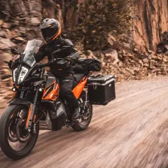 Motociclista en KTM naranja y negra, equipada para aventura, recorre un camino de tierra. La mejor moto trail media cilindrada lista para la exploración.