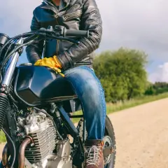 Motociclista con chaqueta de cuero y guantes amarillos, listo para la aventura. ¿Dyneema vs Kevlar? ¡La carretera espera!
