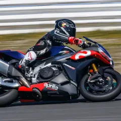 Piloto en una Aprilia RSV4 1100 en circuito, con traje de cuero negro y rojo, casco Shark.