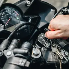 Mano girando la llave de contacto de una moto, pero no enciende. El tablero y las llaves están visibles.