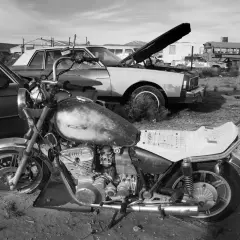 Una moto vieja y un coche en un desguace. ¿Como saber si una moto esta dada de baja? Busca señales de óxido y piezas faltantes.