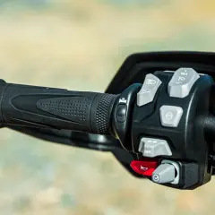 Mandos de la moto: puño negro texturizado y panel de control con botones grises y rojos para luces, crucero y bocina.