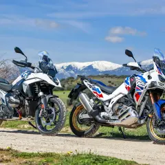 Dos motos de aventura, una Honda Africa Twin 2026 y otra blanca, aparcadas en un camino rural con montañas nevadas al fondo.
