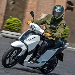 Hombre en scooter Peugeot Tweet 125, con casco y chaqueta verde, circulando por una calle.
