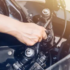 Mano girando la llave de contacto, pero la moto no arranca. El sol ilumina el manillar.