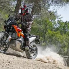 Motociclista con casco y equipo de aventura, derrapando una KTM 490 Adventure en un camino de tierra con polvo levantándose.