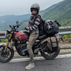 Motociclista con su equipada Triumph Tiger 400, lista para la aventura en una carretera con vistas al mar y montañas.