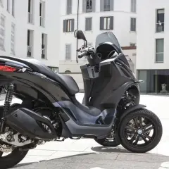 Un Piaggio MP3 300 negro aparcado en una plaza urbana. Su diseño de tres ruedas ofrece estabilidad y un consumo eficiente.