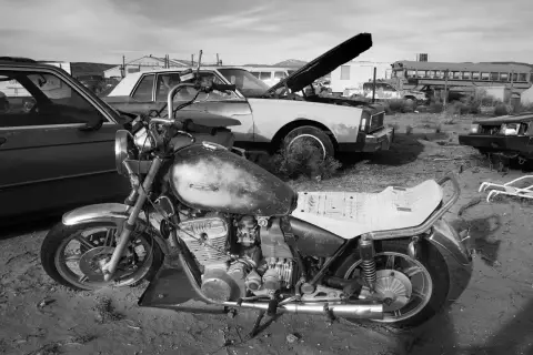 Una moto vieja y un coche en un desguace. ¿Como saber si una moto esta dada de baja? Busca señales de óxido y piezas faltantes.