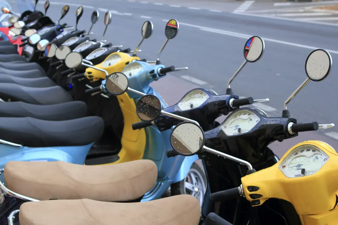 Línea de motos y scooters de colores aparcadas en la calle. Para saber si una moto está libre de cargas, revisa su documentación.