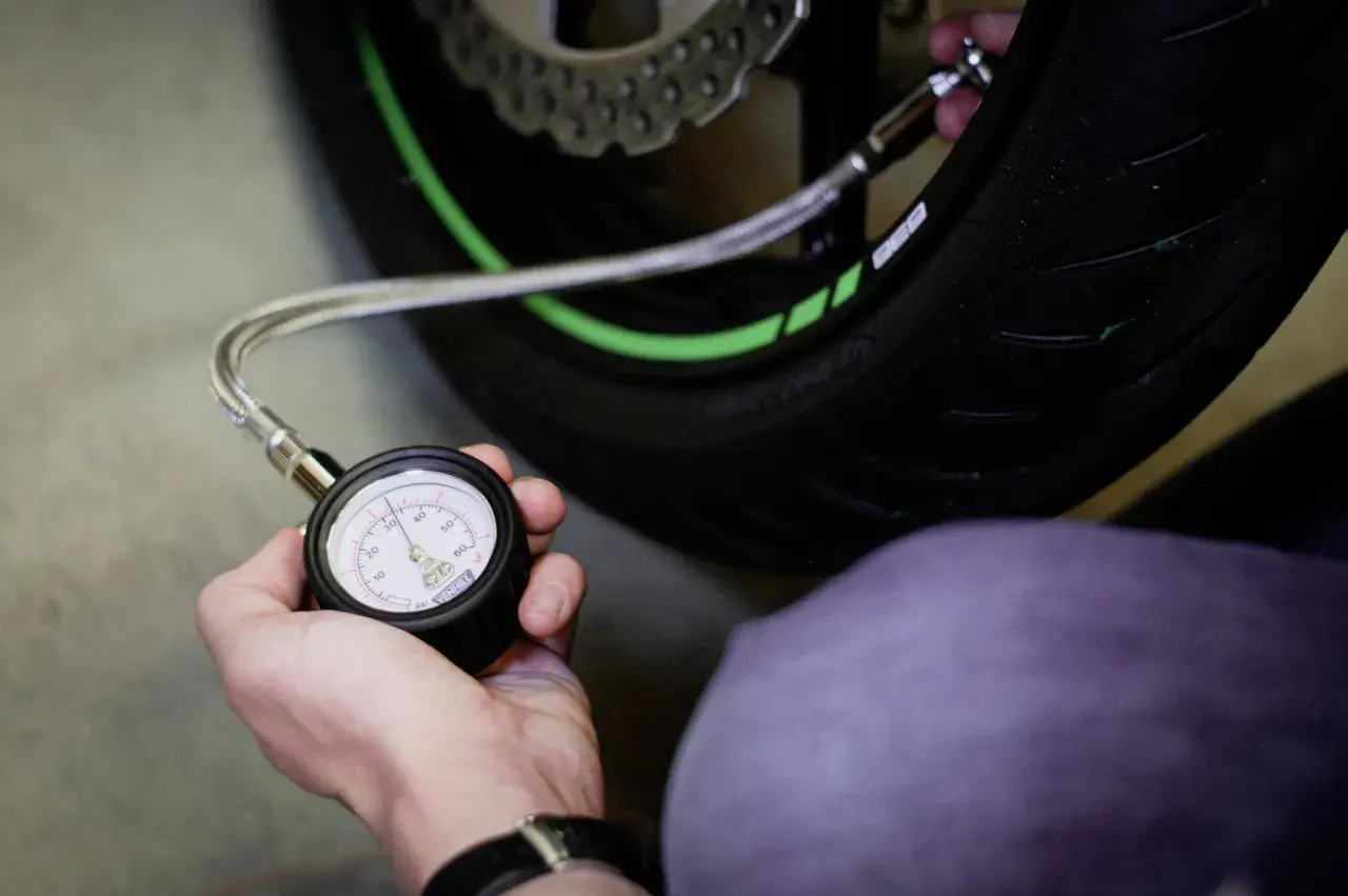 Mano revisando la presión neumaticos moto con un manómetro. El neumático tiene detalles verdes.