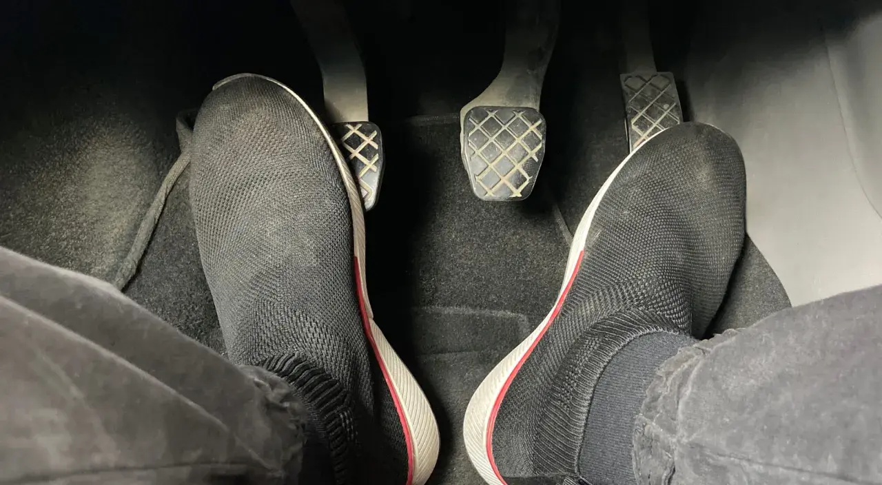 Pies con zapatillas negras listas para arrancar. Hay que pisar el embrague para arrancar el coche.