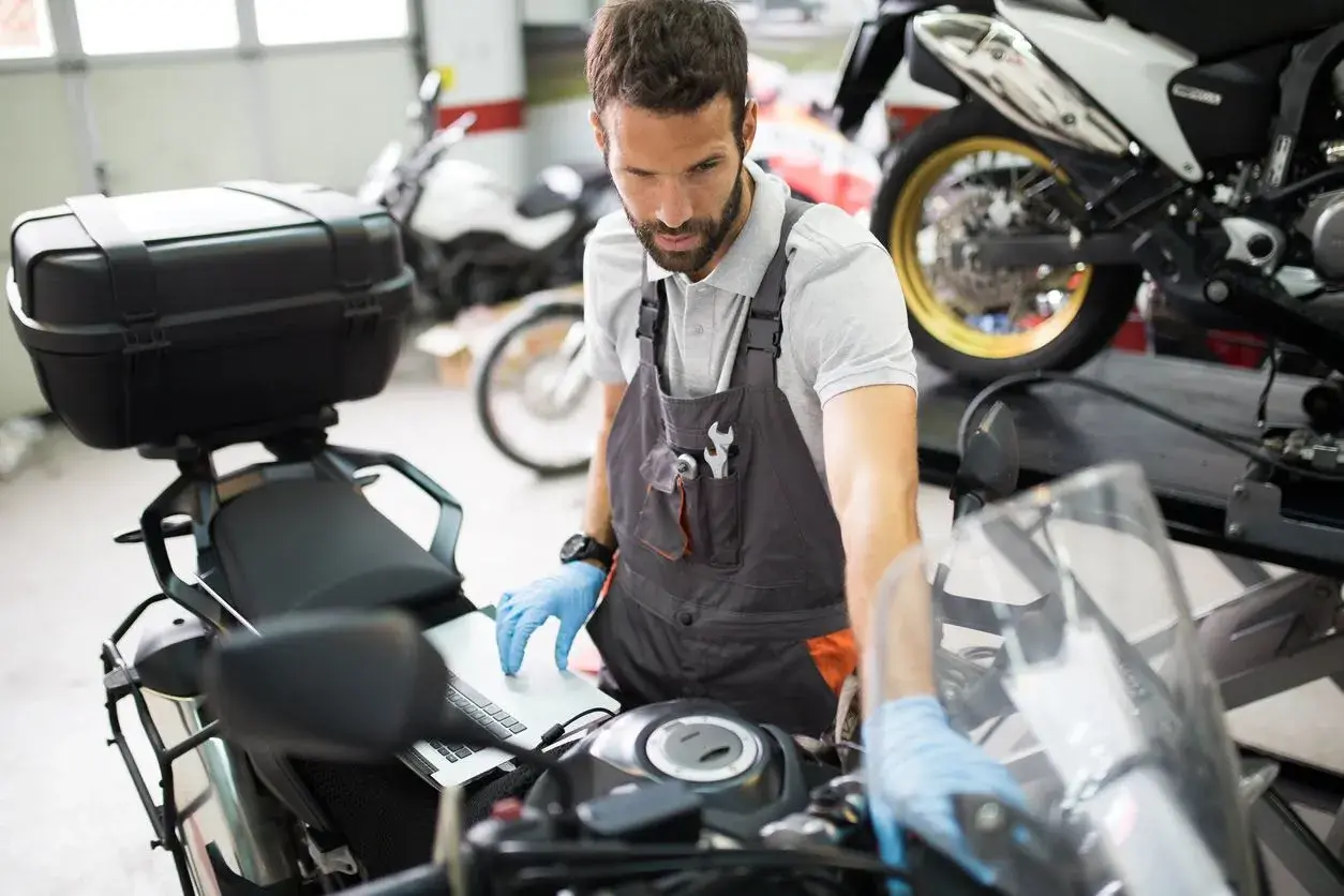 Mecánico revisa en laptop por qué la moto se para en marcha y no arranca.
