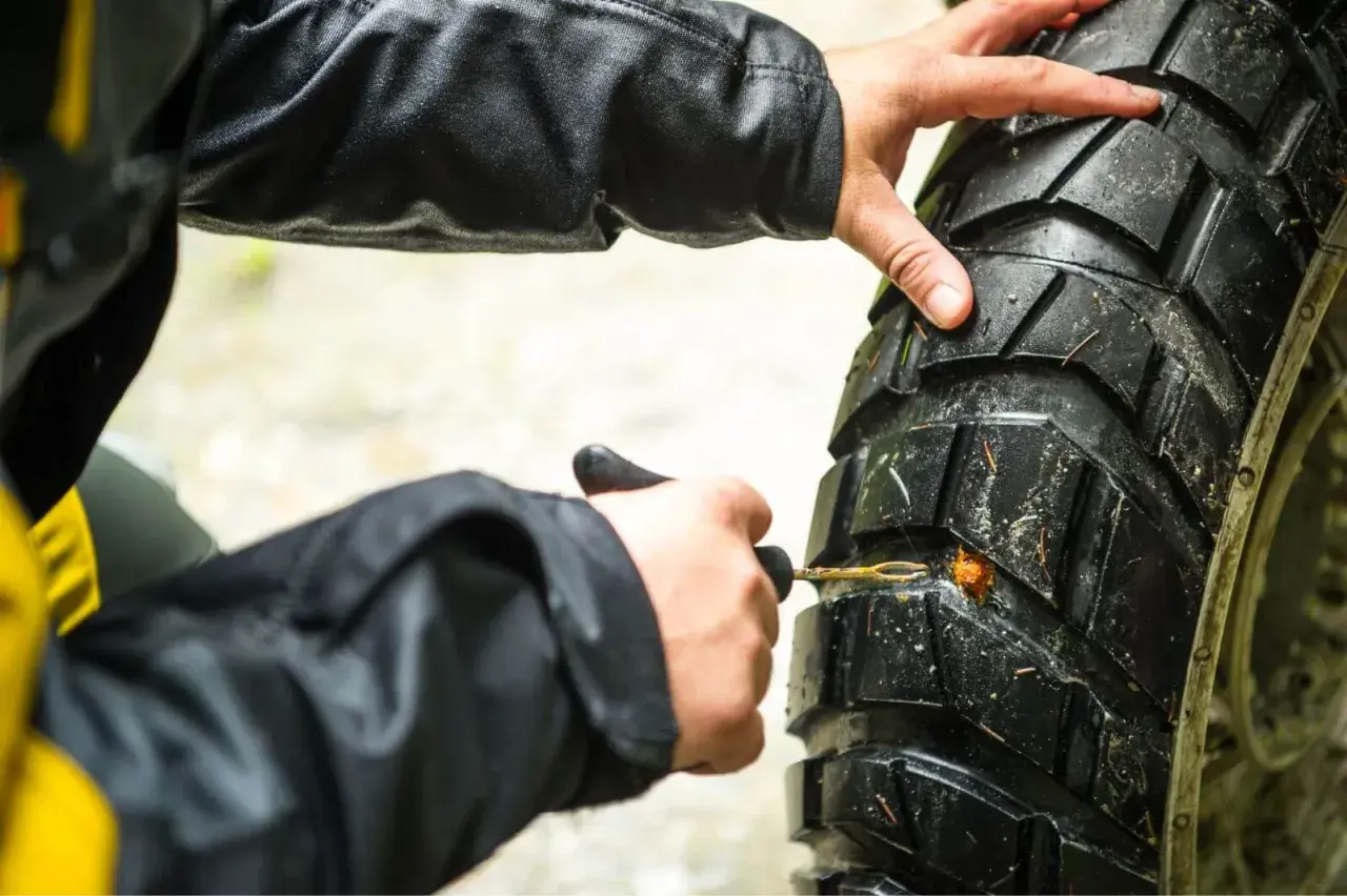 Manos arreglando pinchazo moto con kit de reparación.