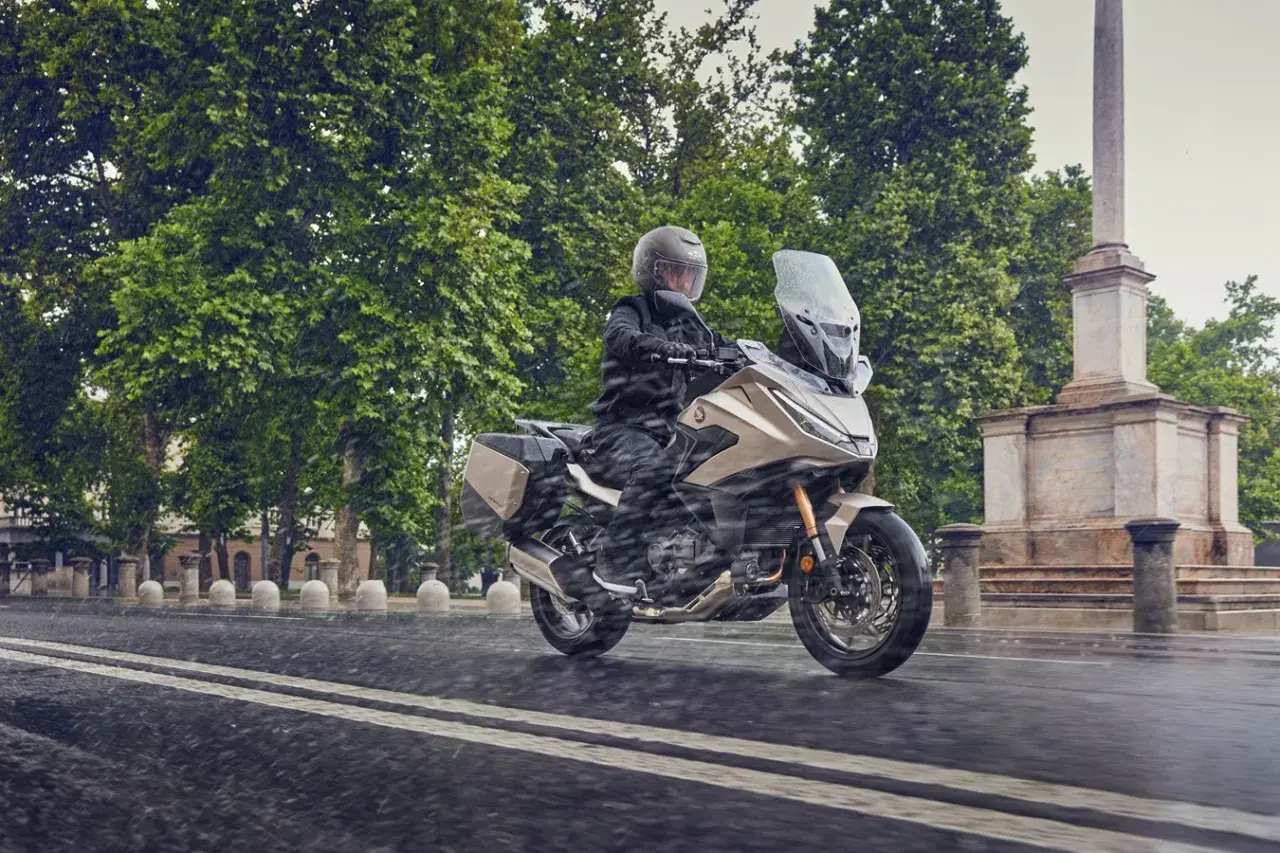 Motociclista en moto beige con alforjas, rodando bajo la lluvia. ¿Cuántos kilómetros dura una moto 125? ¡Esta parece lista para un largo viaje!