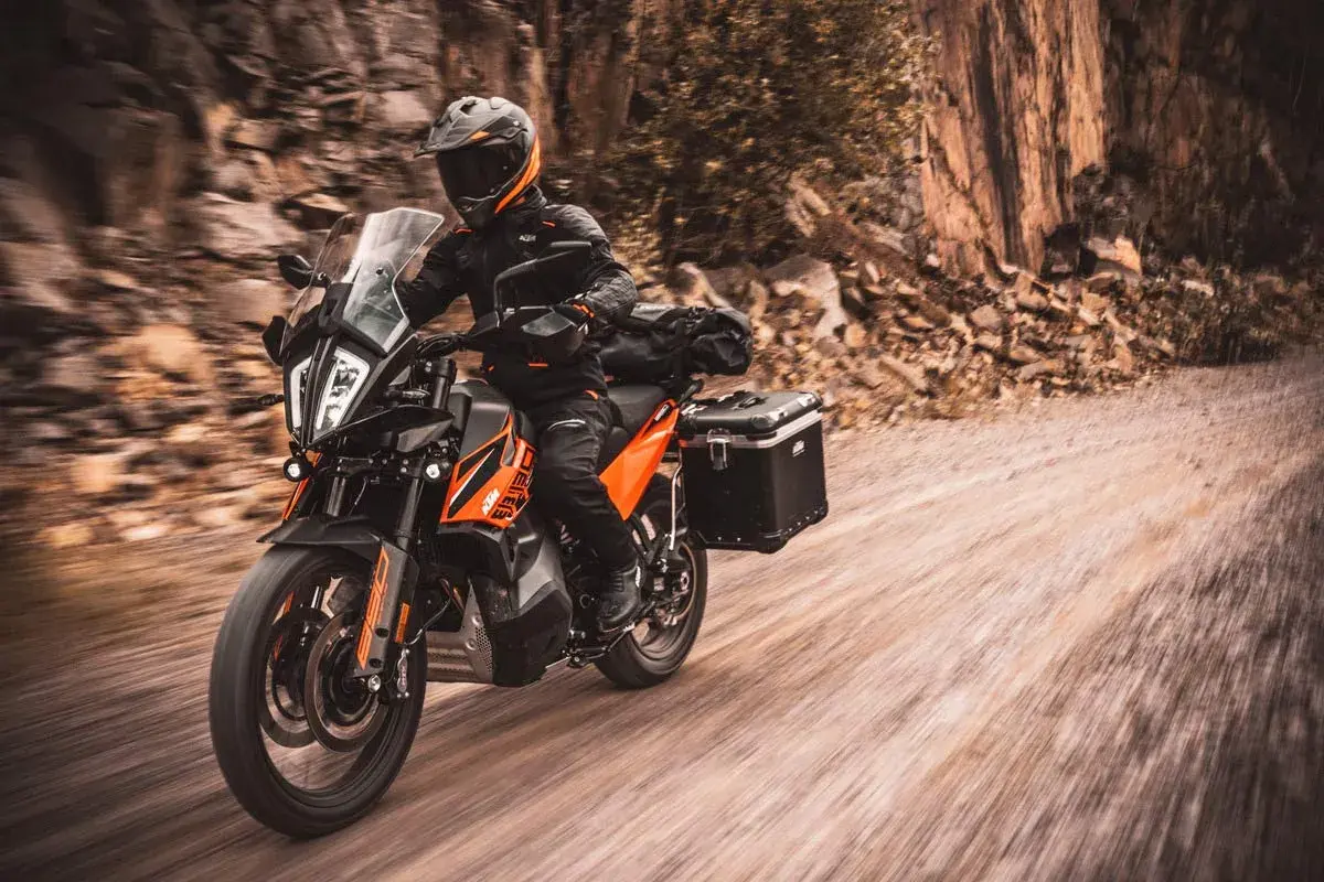 Motociclista en KTM naranja y negra, equipada para aventura, recorre un camino de tierra. La mejor moto trail media cilindrada lista para la exploración.
