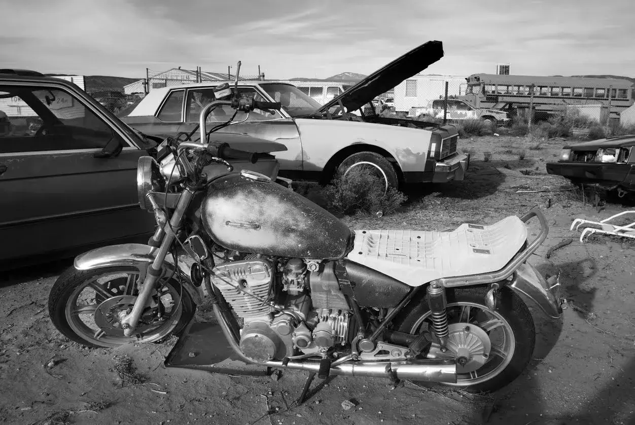 Una moto vieja y un coche en un desguace. ¿Como saber si una moto esta dada de baja? Busca señales de óxido y piezas faltantes.