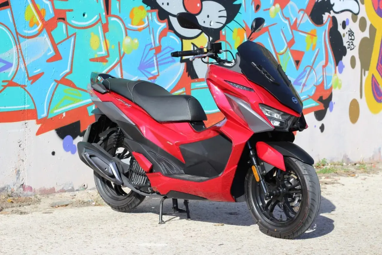Scooter SYM Jet X 125 rojo brillante, con diseño deportivo, frente a un muro con grafitis coloridos. ¡Un estilo que inspira buenas opiniones!