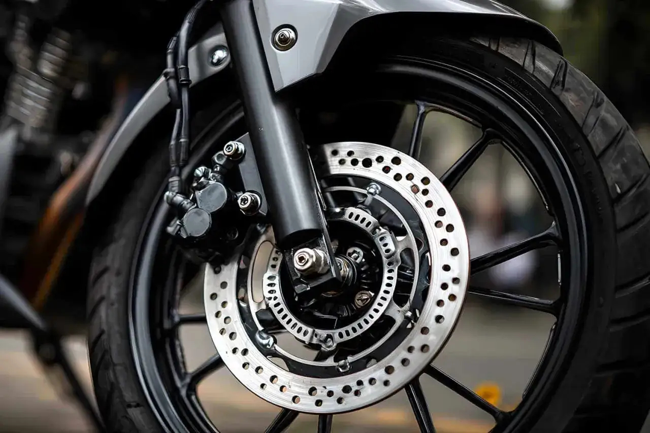 Primer plano de la rueda delantera de una motocicleta, mostrando el disco de freno perforado y la pinza. Esto ayuda a entender cuál es el freno motor.
