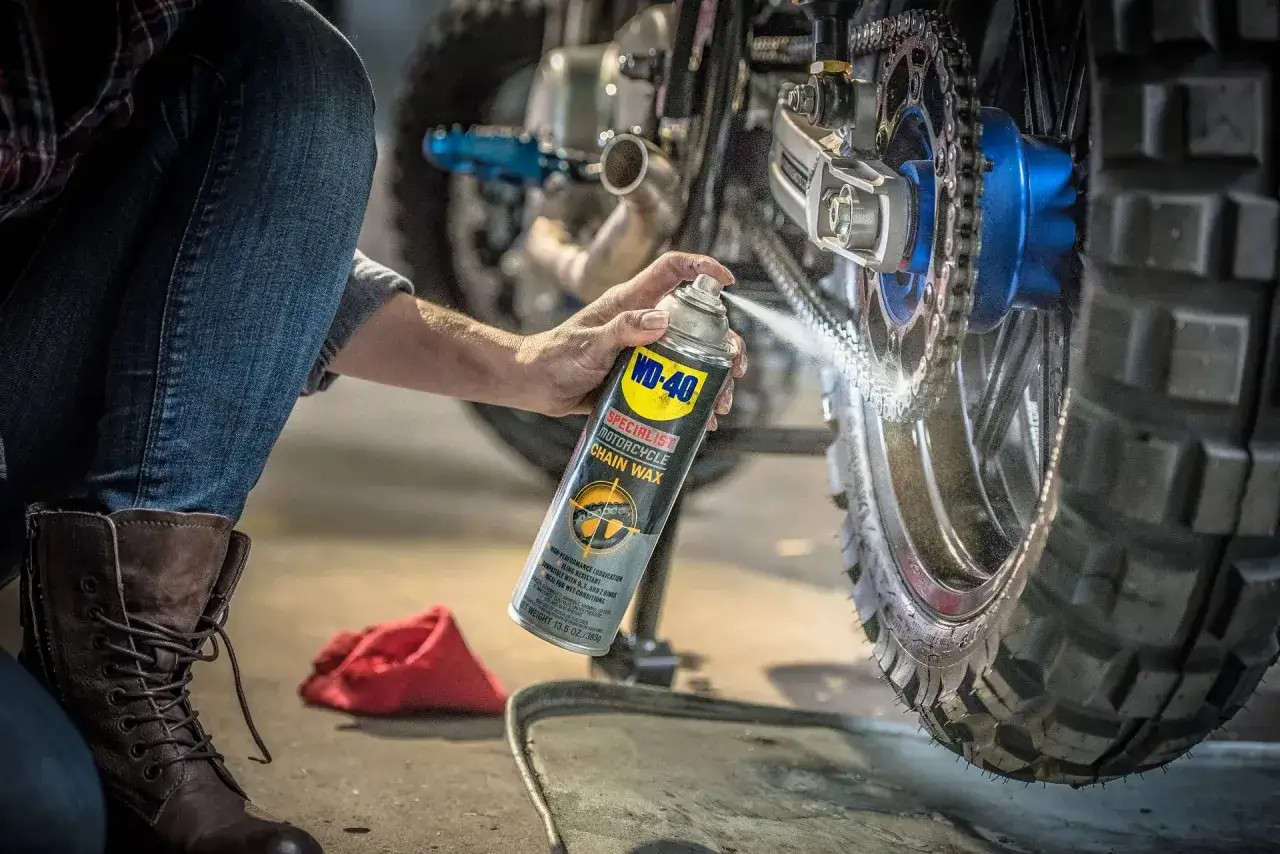 Persona en cuclillas aplica cera a la cadena de una moto para engrasarla.