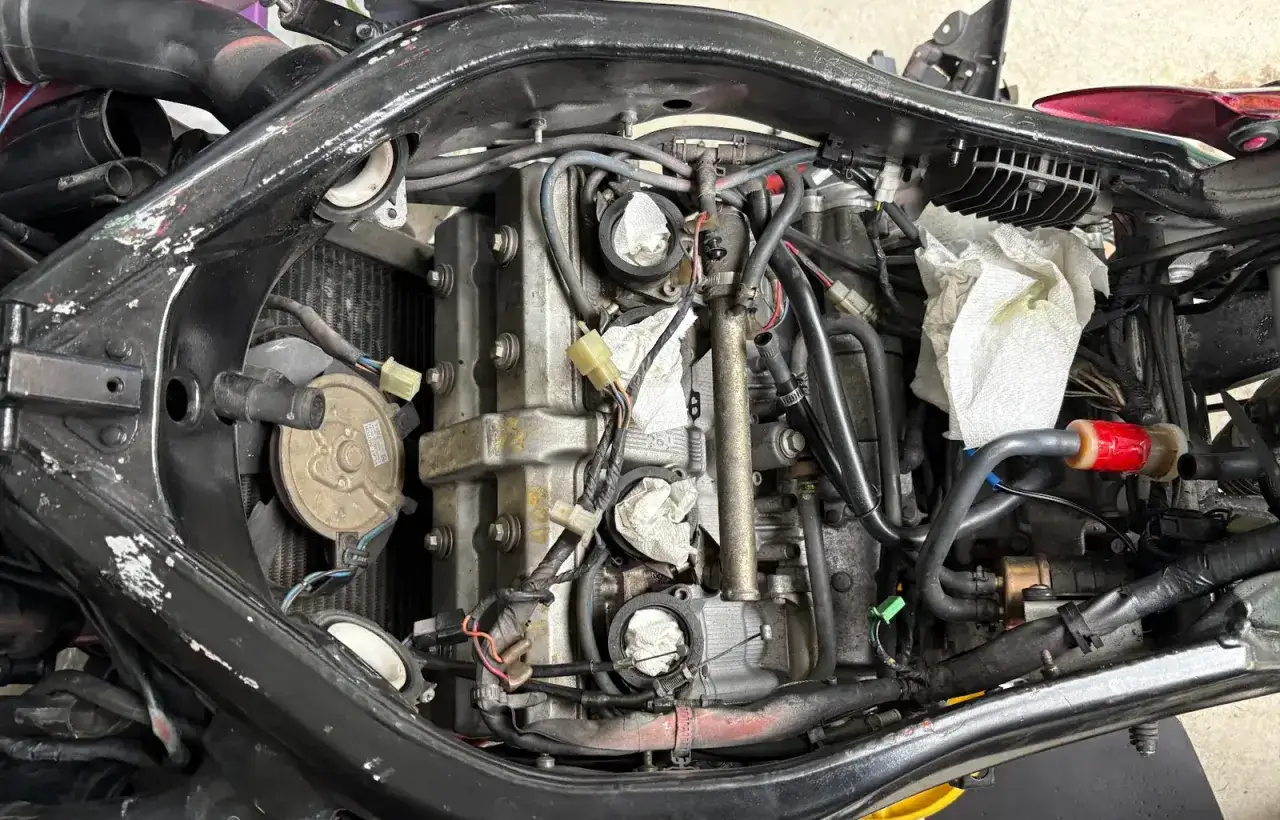 Motor de moto desmontado, con cables, mangueras y radiador visibles. Parece que la moto no arranca y se está revisando el motor.