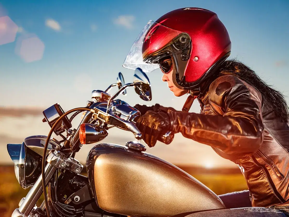 Mujer con casco rojo y chaqueta de cuero sobre una moto, sintiendo la libertad de las mejores motos del mundo.