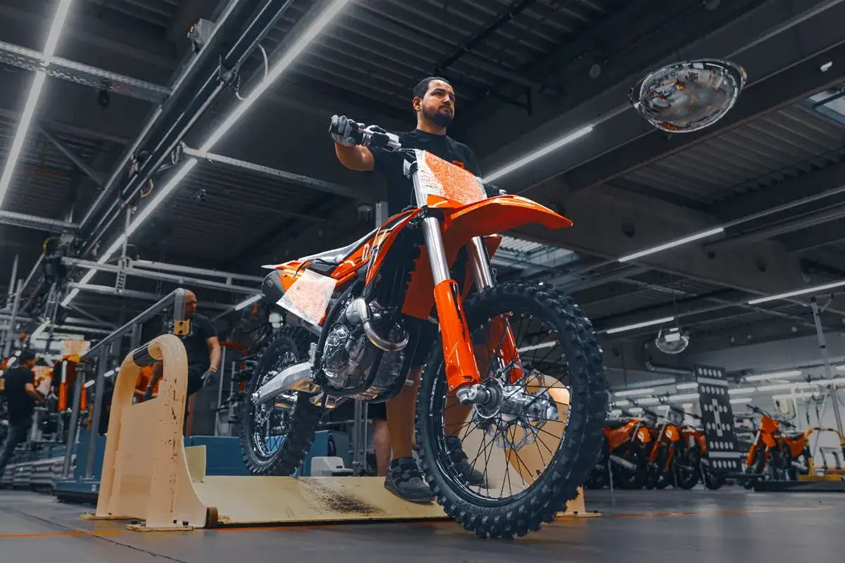 Hombre en fábrica con moto KTM naranja. ¿KTM de donde es? De Austria, ¡pura potencia!