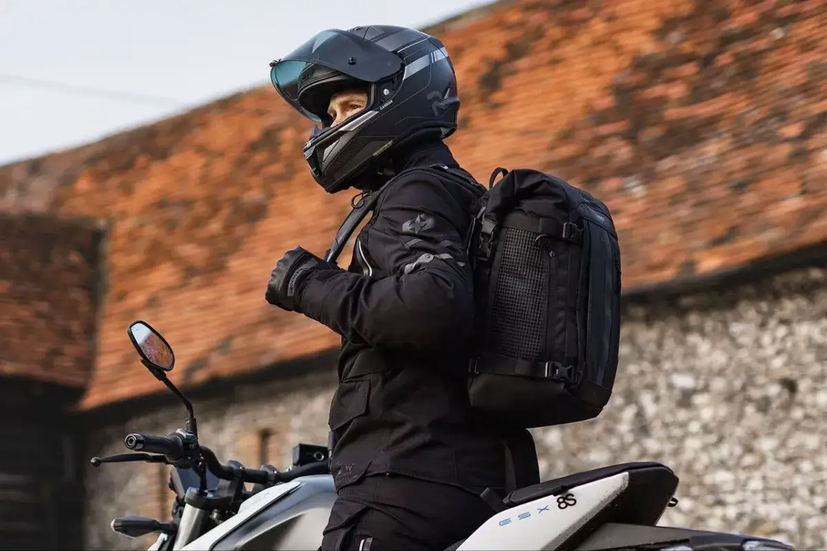 Motociclista con casco y chaqueta negra, listo para viajar. Se puede llevar mochila en moto, como demuestra este modelo con una mochila negra bien ajustada.