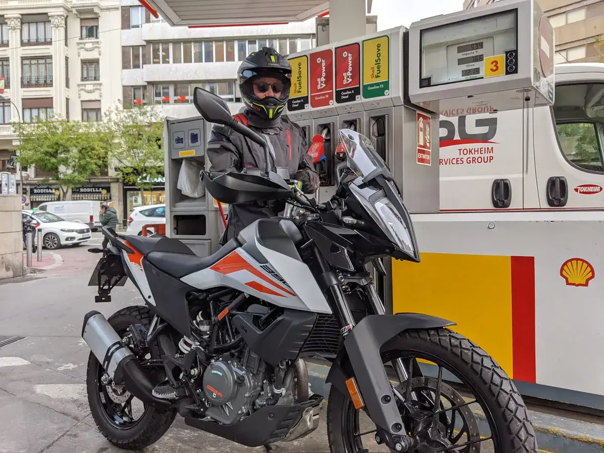 Motociclista con casco y chaqueta repostando gasolina a su moto en una gasolinera Shell.