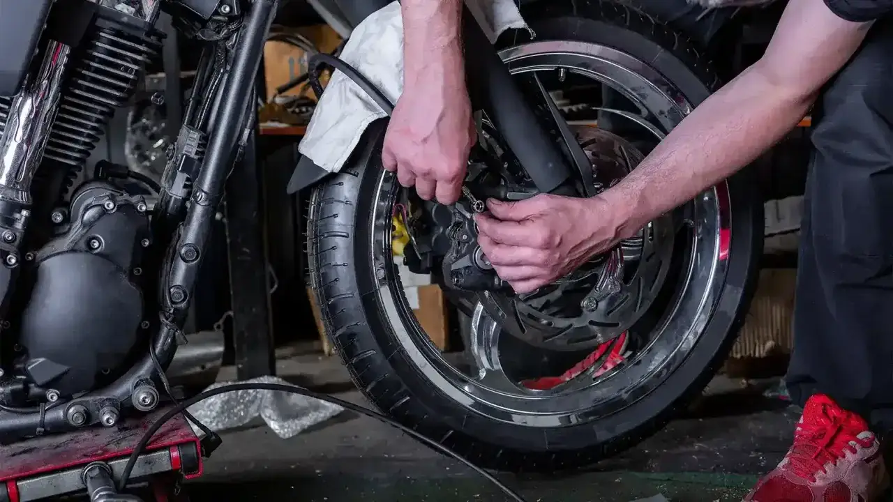 Manos trabajando para reparar rueda de motocicleta. Se ve el motor, la llanta cromada y el disco de freno.