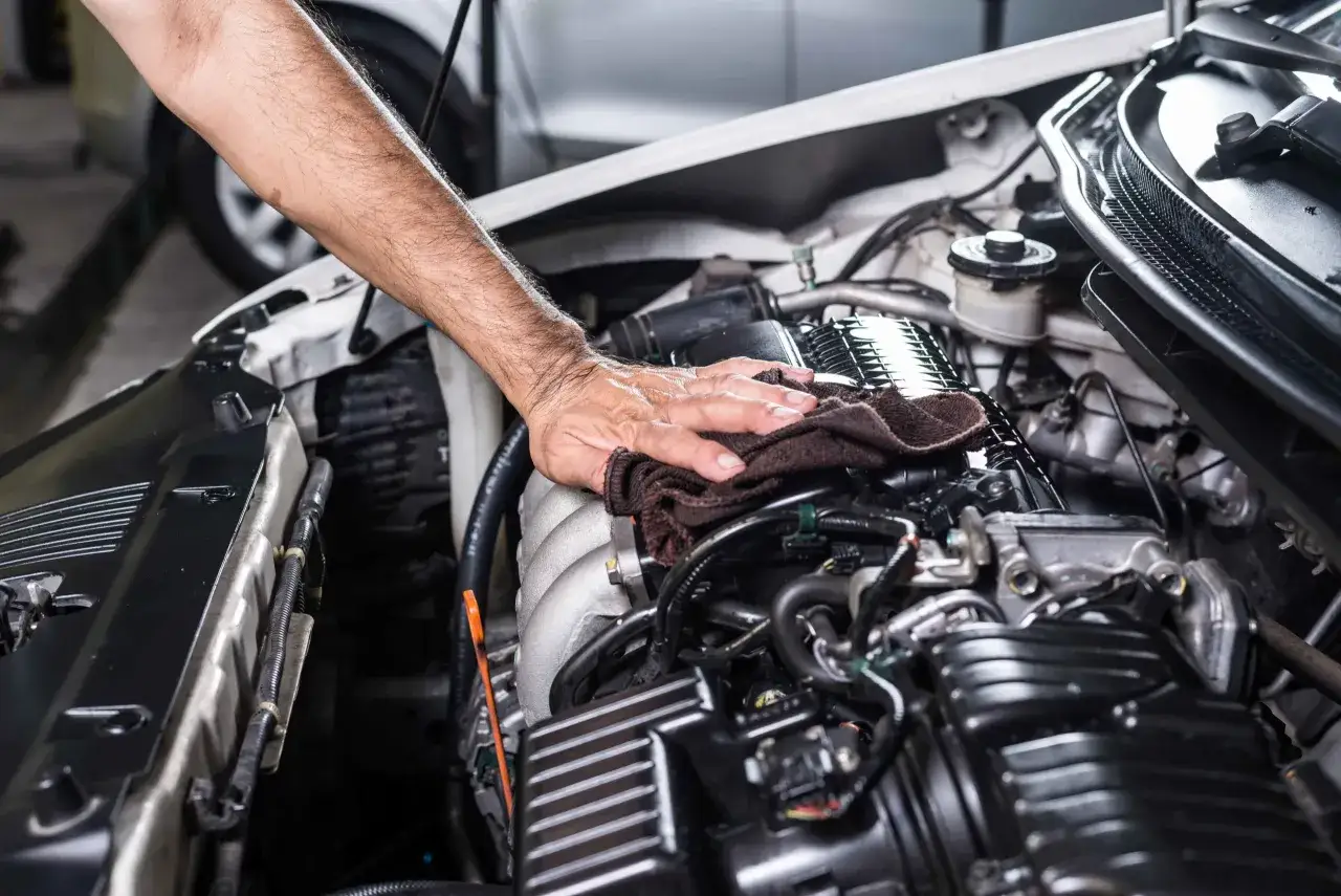 Mano limpiando el motor de un coche con cuatro cilindros.