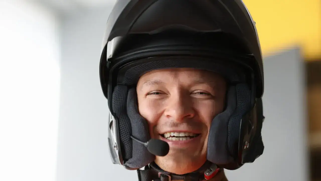 Hombre sonriente con casco de moto y micrófono, listo para usar su intercomunicador moto legal.