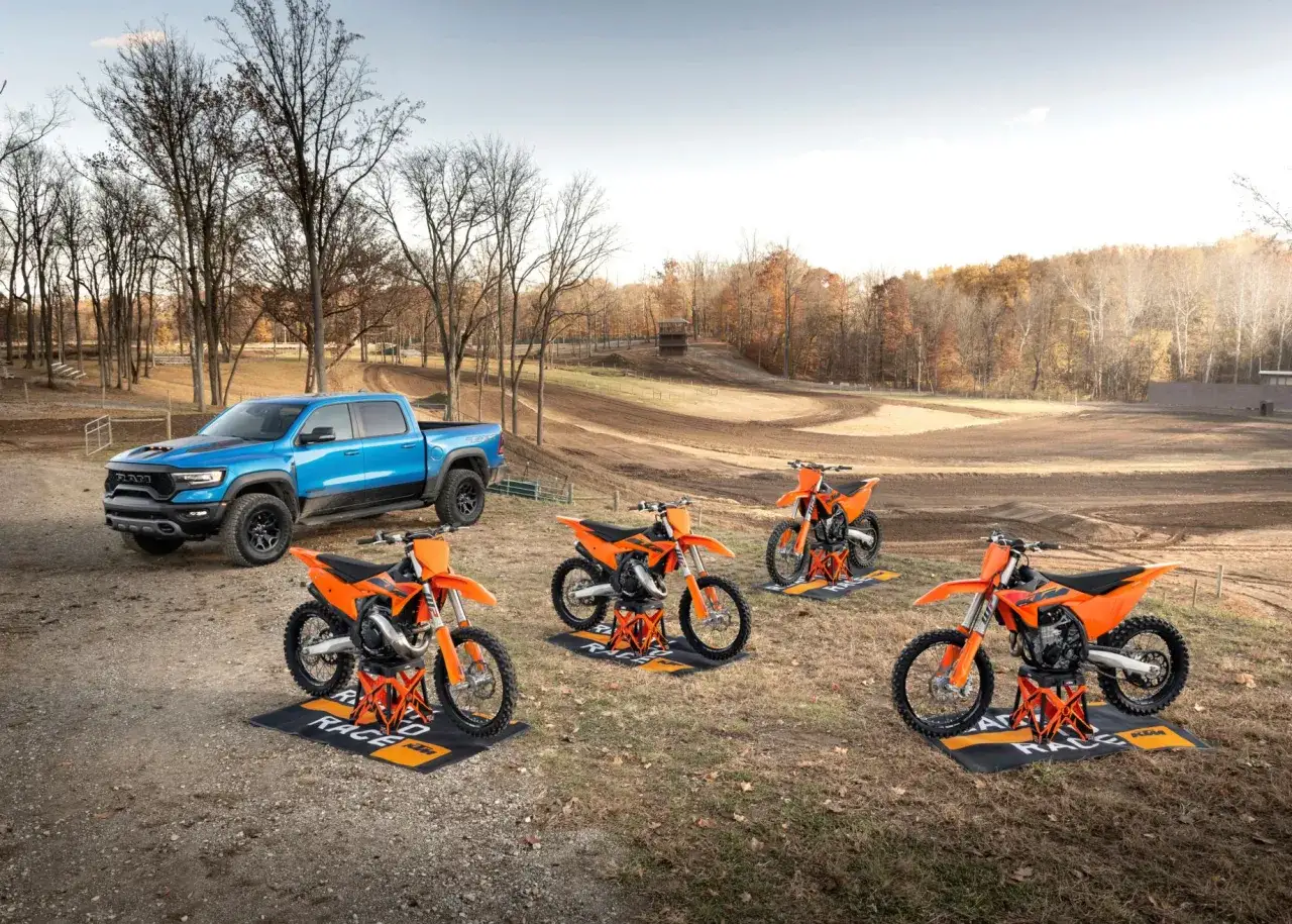 Camioneta azul y motos KTM naranjas listas para la acción en una pista de motocross. ¡Noticias frescas para los amantes de la velocidad!