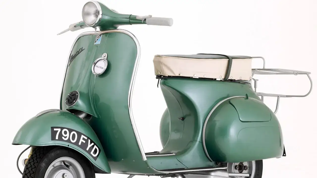 Un clásico verde de los modelos Vespa años 60, con su asiento de dos tonos y portabultos cromado, listo para un paseo nostálgico.