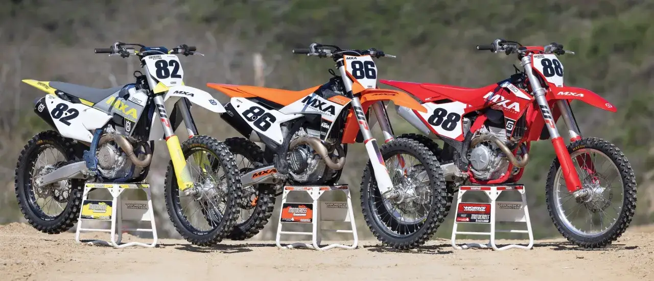 Tres motos de cross, una blanca y amarilla con el número 82, una naranja con el 86 y una roja con el 88, listas para la acción de pierer mobility.