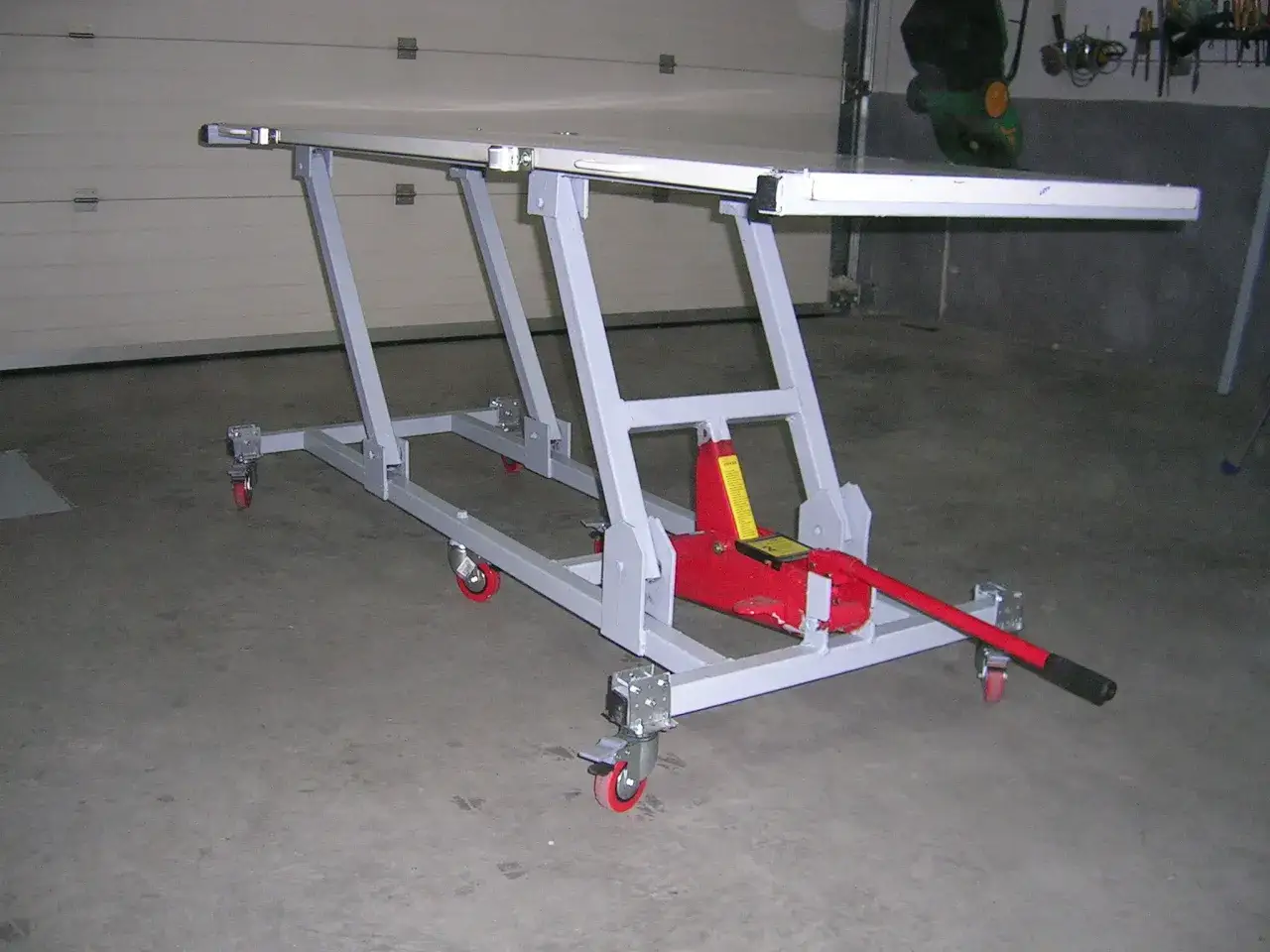 Elevador moto casero con gato hidráulico rojo y ruedas. Ideal para reparaciones.