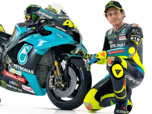 Valentino Rossi posa junto a su moto de competición, luciendo su icónico traje de carreras.